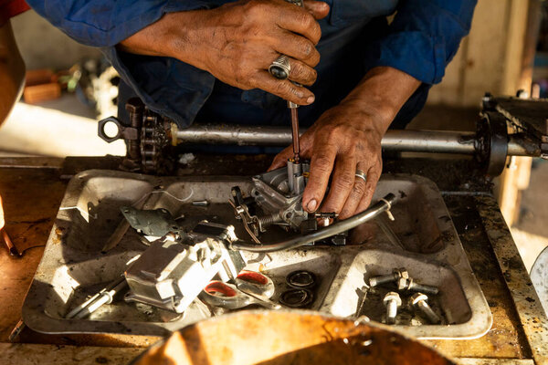 Waisai, Indonesia - Oct 16, 2019: A man, who works as a mechanic, skillfully fixes the carburetor of a boat engine in his workshop