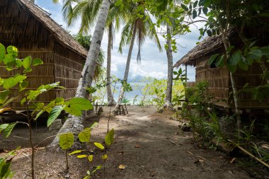Geleneksel olarak Gam Adası, Raja Ampat, Endonezya 'da tropikal bir plaj yakınlarında palmiye ağaçları arasında küçük kulübeler inşa edilir.