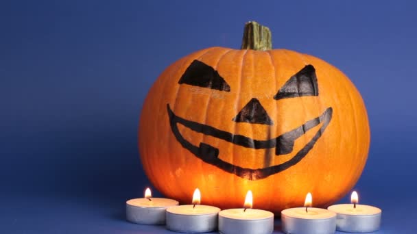 Halloween pompoen of jack-o-lantaarn met gloeiende ogen op een blauwe achtergrond. jack-o-lantaarn voor een Halloween feest staat op een tafel tegen een donkere achtergrond. — Stockvideo