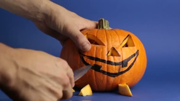 Een jonge meester maakte een jack-o-lantaarn voor het Halloween feest. Een jongeman snijdt een halloween pompoen of jack-o-lantaarn met gloeiende ogen. Voorbereiden om Halloween te vieren. — Stockvideo