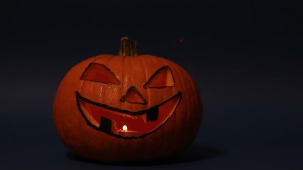 Calabaza de Halloween o Jack-o-linterna con ojos brillantes sobre un fondo azul. jack-o-lantern para una fiesta de Halloween se levanta sobre una mesa sobre un fondo oscuro. — Vídeo de stock