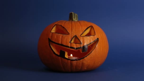 Zucca di Halloween o jack-o-lanterna con gli occhi luminosi su uno sfondo blu. jack-o-lanterna per una festa di Halloween si erge su un tavolo su uno sfondo scuro. — Video Stock