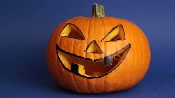 Jack-o-lantern for a Halloween party stands on a table against a dark background. Halloween pumpkin or jack-o-lantern with glowing eyes on a blue background. — Stock Video