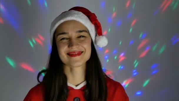 El retrato de cerca de una joven mujer feliz, ella en un ambiente festivo se prueba un disfraz de Santa Claus, preparándose para el nuevo año. Mujer atractiva joven en un traje de año nuevo sonríe ampliamente contra el — Vídeos de Stock