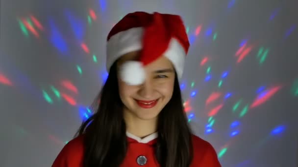 Hezká mladá žena v klobouku Santa Clause se usmívá a koketně se dívá do kamery. Novoroční prázdniny. — Stock video