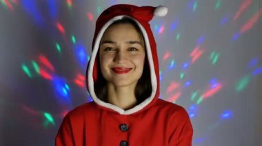 Genç mutlu bir kadının yakın plan portresi, neşeli bir ruh hali içinde Noel Baba kostümü deniyor, Noel için hazırlanıyor. Yeni yıl kostümü içinde genç çekici bir kadın gülümseyerek...
