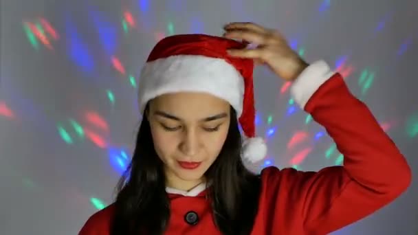 Jolie jeune femme en santa claus chapeau souriant et regardant coquettishly la caméra. Nouvel an vacances. — Video