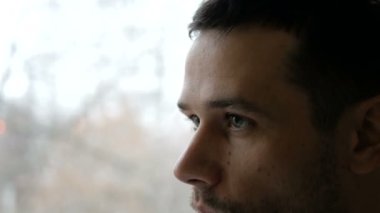 Genç ve çekici bir adam beyaz bir fincandan kahve içip pencereden dışarı bakıyor..