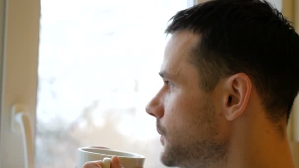 Nahaufnahme eines jungen Mannes, der in seiner Küche steht und Kaffee aus einer weißen Tasse trinkt. — Stockvideo