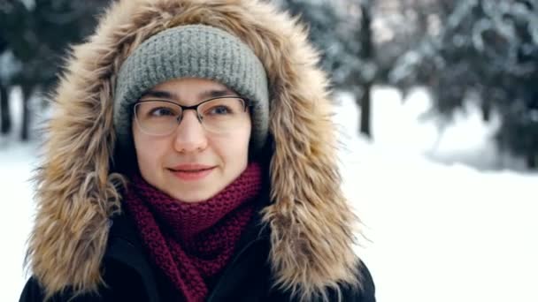 Junge glückliche Frau in romantischer Stimmung beim Spazierengehen im Winterwald. Attraktive Frau mit grünem Hut und flauschiger Kapuze spaziert durch einen verschneiten Park. — Stockvideo