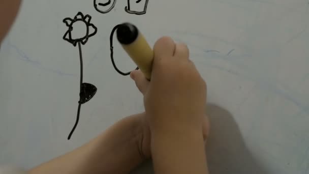 Tekenles op de kleuterschool. Klein aantrekkelijk meisje tekent met een zwarte stift op een wit bord. Close-up van een kleine meisjes hand, ze tekent met een zwarte vlam op een wit bord. — Stockvideo