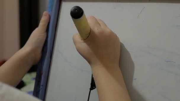Pequeña chica atractiva dibuja con un marcador negro en una pizarra blanca. — Vídeos de Stock