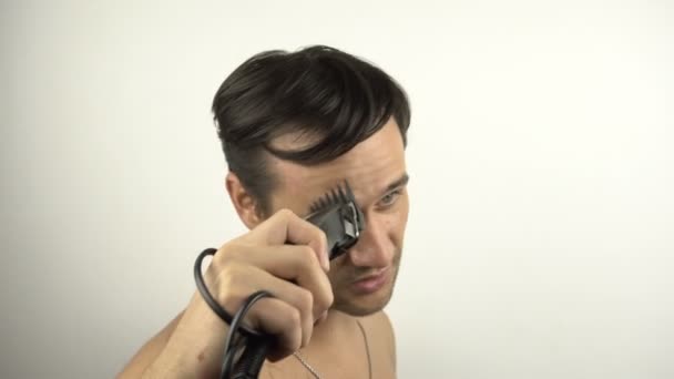 若い魅力的な男は、隔離された自宅に座っている間、ヘアクリップを使用して髪をカットします。若い男は電気トリマーで自分の髪を切ります. — ストック動画