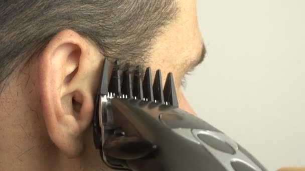Młody atrakcyjny facet obcina włosy za pomocą strzyżenia podczas kwarantanny w domu. Młody facet obcina sobie włosy elektrycznym przycinaczem.. — Wideo stockowe
