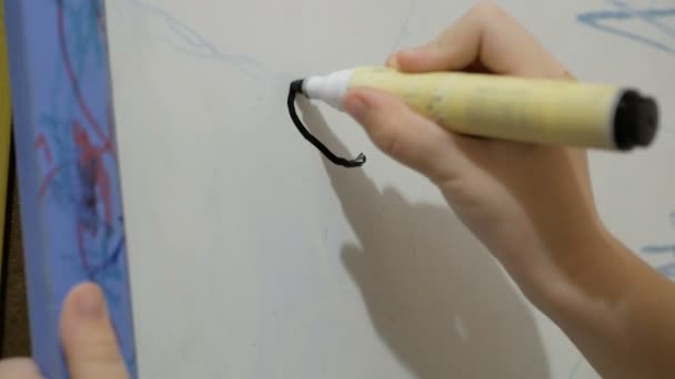 Petite fille attirante dessine avec un marqueur noir sur un tableau blanc. Gros plan d'une petite main de fille, elle dessine avec un flamaster noir sur un tableau blanc. — Video