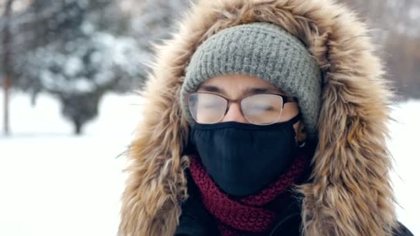 Eine junge attraktive Frau mit Schutzmaske und Brille vor dem Hintergrund eines Winterwaldes. — Stockvideo