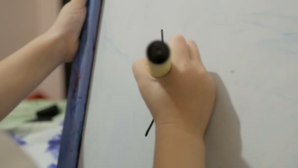 Gros plan d'une petite main de fille, elle dessine avec un flamaster noir sur un tableau blanc. Cours de dessin à la maternelle. — Video