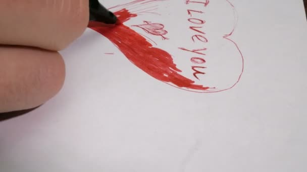 Zbliżenie na dłoń młodego mężczyzny. Zapisuje na papierze słowa "Kocham cię czerwonym długopisem".. — Wideo stockowe