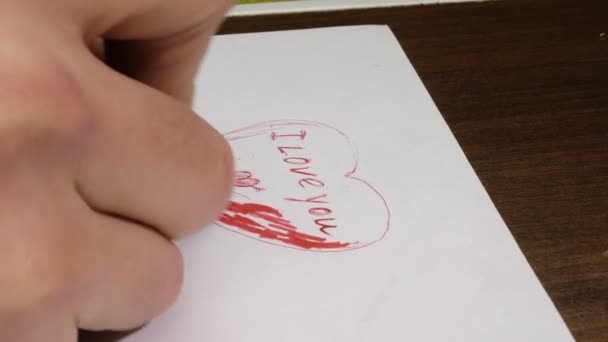Close-up de um jovem homem mão ele escreve no papel as palavras que eu te amo com uma caneta vermelha. — Vídeo de Stock