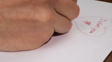 Genç bir adam kız arkadaşı için sevgililer günü kartı çekiyor. Sevgililer günü için tebrik kartı hazırlıyor..
