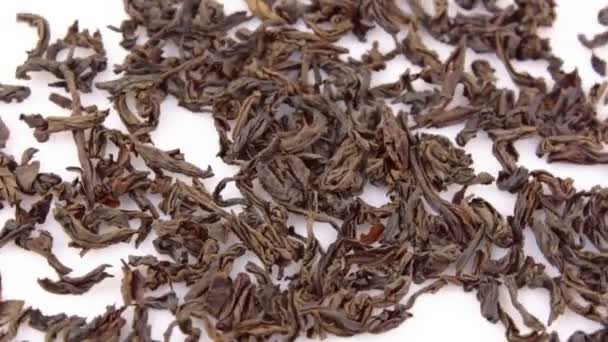 Primer plano de una rotación de té negro de hoja grande sobre un fondo blanco. Las hojas secas de té negro rotan en un plato. Un puñado de grandes hojas de té negro gira en un plato blanco. — Vídeos de Stock