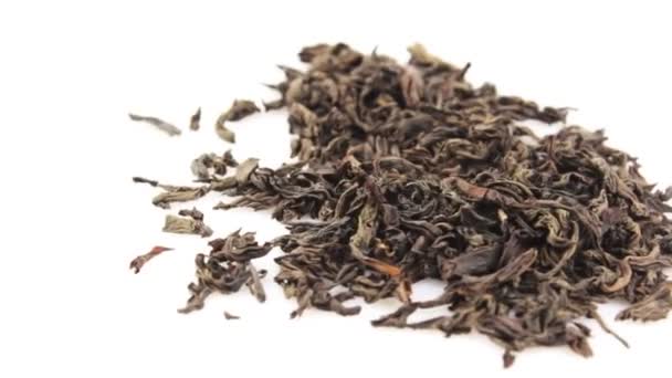 Primer plano de una rotación de té negro de hoja grande sobre un fondo blanco. Las hojas secas de té negro rotan en un plato. Un puñado de grandes hojas de té negro gira en un plato blanco. — Vídeo de stock