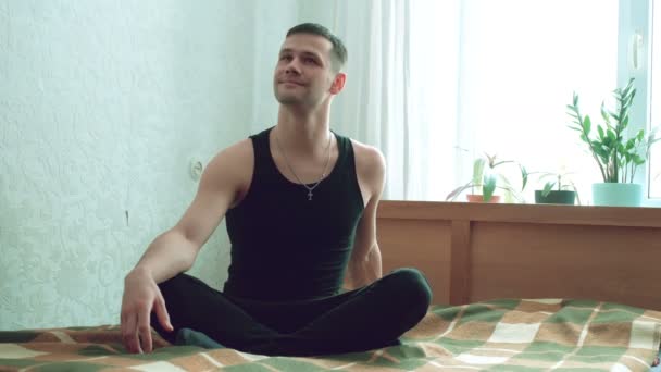 若い魅力的な男は彼のリビングルームのベッドで瞑想しています. — ストック動画