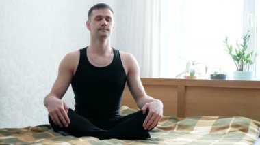 Genç adam evde meditasyonun tadını çıkarıyor. Genç ve çekici bir adam oturma odasında yatakta meditasyon yapıyor. Sağlıklı yaşam tarzı konsepti..