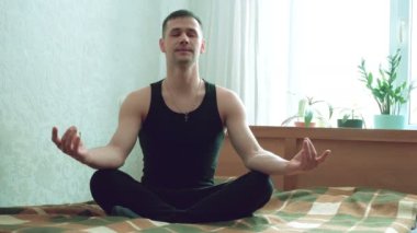 Genç adam evde meditasyonun tadını çıkarıyor. Genç ve çekici bir adam oturma odasında yatakta meditasyon yapıyor..