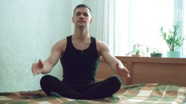 Genç ve çekici bir adam oturma odasında yatağında oturmuş Assanas taklidi yapıyor. Genç ve mutlu bir adam evdeki yatakta lotus pozisyonunda otururken meditasyon yapıyor. Genç adam nefes egzersizi yapıyor.