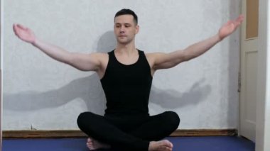 Genç ve mutlu bir adam evde yoga minderinin üzerinde lotus pozisyonunda meditasyon yapıyor. Genç adam evde yoga ve meditasyon yapıyor. Sağlıklı yaşam tarzı kavramı. Genç ve çekici bir adam assanas çalıyor.