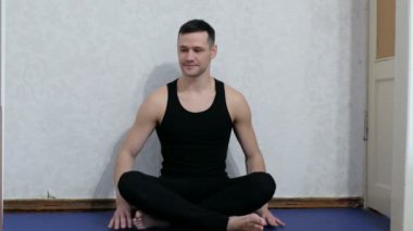 Genç ve mutlu bir adam evde yoga minderinin üzerinde lotus pozisyonunda meditasyon yapıyor. Genç adam evde yoga ve meditasyon yapıyor. Sağlıklı yaşam tarzı kavramı. Genç ve çekici bir adam assanas çalıyor.