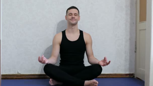 El joven está haciendo yoga y meditando en casa. Joven hombre feliz haciendo meditación sentado en posición de loto en la esterilla de yoga en casa. Concepto de estilo de vida saludable. Joven atractivo hombre realiza assanas — Vídeos de Stock