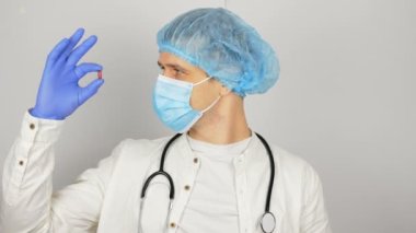 Tıbbi maskeli genç bir doktor elinde yeni bir ilaç sunan kırmızı bir hap tutuyor. Genç bir doktor sunumda yeni bir ilaç gösteriyor, tüm hastalıklar için kırmızı bir hap..