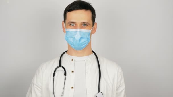 Un joven médico guapo con una máscara médica tiene una píldora roja en sus manos que presenta un nuevo fármaco. Un joven médico muestra un nuevo fármaco en la presentación, una píldora roja para todas las enfermedades. — Vídeos de Stock