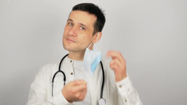 En ung, kjekk lege tar av seg sin medisinske beskyttelsesmaske og sukk. – stockvideo