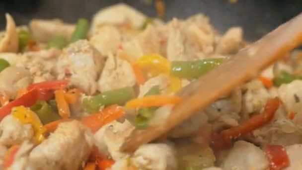 El chef mezcla pollo con verduras en una sartén. Un chef profesional prepara kritsa con verduras en un wok. El filete de pollo jugoso se fríe en un wok con verduras frescas. — Vídeo de stock