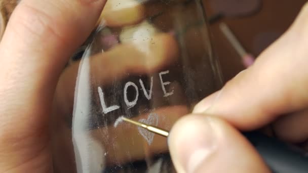 Der Meister graviert das Wort Liebe auf das Glas. Großaufnahme der Hand eines Meisters, der das Wort Liebe und ein Herzsymbol auf das Glas graviert. — Stockvideo