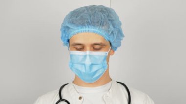 Tıbbi maskeli genç ve yakışıklı bir doktor elinde kırmızı bir hap tutuyor ve yeni bir ilaç sunuyor..