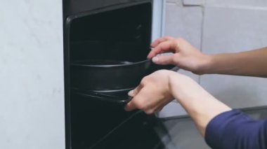 Genç bir kadının yakın plan çekimi fırına turta koyuyor. Genç bir kadının elleri fırına hamur dolu bir yemek tepsisi koydu..