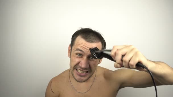 Muž si oholí hlavu a hlasitě křičí, když se dívá do zrcadla. Mladý vtipálek před zrcadlem si holí vlasy stříháním vlasů, zatímco sedí doma v karanténě.. — Stock video