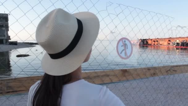 Junge schöne Frau mit weißem Hut blickt auf den versunkenen Öltanker. Junge attraktive Frau mit weißem Hut blickt traurig auf den versunkenen Tanker, der am Ufer liegt. Umweltkatastrophe. — Stockvideo