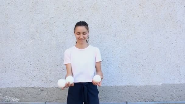 En attraktiv jonglör tränar sina jongleringsfärdigheter. Professionell cirkusartist jonglerar med vita bollar på gatan. En professionell jonglör jonglerar med vita bollar. — Stockvideo