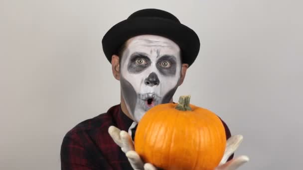 A terrible man in clown makeup and with a pumpkin on his head grimaces and waves his hand in greeting to his victim. A scary clown with a pumpkin on his head grimaces and laughs terribly. Halloween — Stock Video