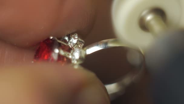 De juwelier is bezig met het snijden van een edelsteen op een gouden ring. Een professionele juwelier polijst een rode edelsteen op een gouden ring met behulp van een speciaal gereedschap.Verwerking van sieraden, polijsten van een edelsteen door — Stockvideo