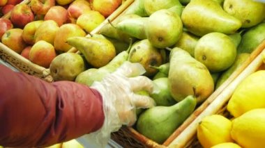 Koruyucu eldiven giymiş genç kadınlara yaklaşırken süpermarketten olgun organik armutları topluyor. Genç ve çekici bir kadın karantina sırasında marketten olgun organik armutları topluyor. Genç bir kadın.