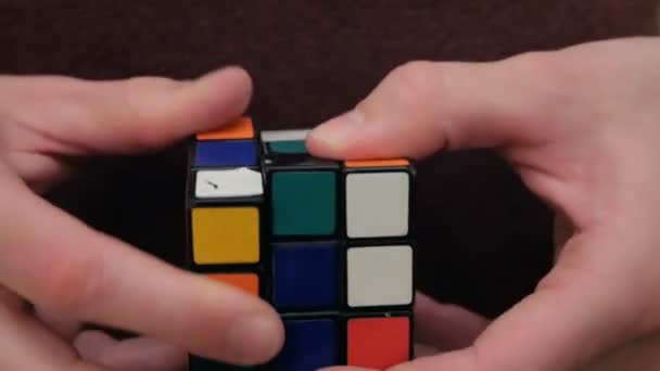 Ein junger Mann löst ein Rätsel, trainiert, um einen Rubiks-Würfel zu sammeln. Ein junger attraktiver Kerl sammelt einen Rubiks-Würfel. Nahaufnahme eines jungen Mannes, der versucht, einen Rubiks-Würfel zu lösen. — Stockvideo