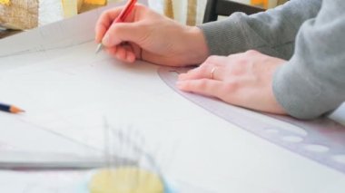 Genç bayan moda tasarımcısı yeni bir elbise modeli çiziyor. Genç bir moda tasarımcısının eli, yeni bir elbise modelini kesmekle meşgul. Moda.