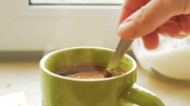 Şefkatli genç bir ev hanımı sıcak aromatik kahveyle bir fincanda şeker karıştırıyor. Genç ve çekici bir kadının elinin yakın plan fotoğrafı. Şekeri aromalı doğal kahveyle karıştırıyor..