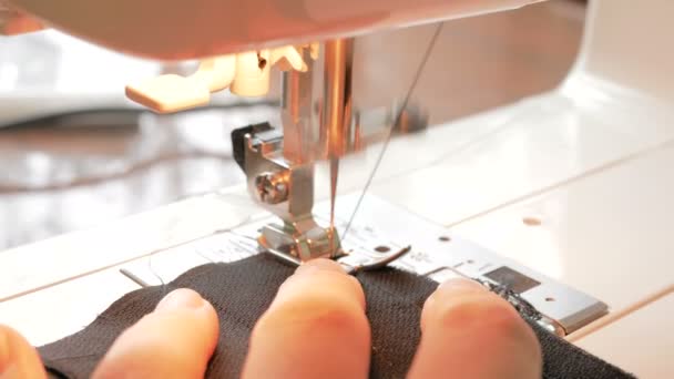 Una joven ama de casa cariñosa cose máscaras protectoras usando una máquina de coser. Primer plano de la mano de una joven y atractiva voluntaria, cose máscaras protectoras médicas durante la cuarentena. Primer plano de un — Vídeo de stock